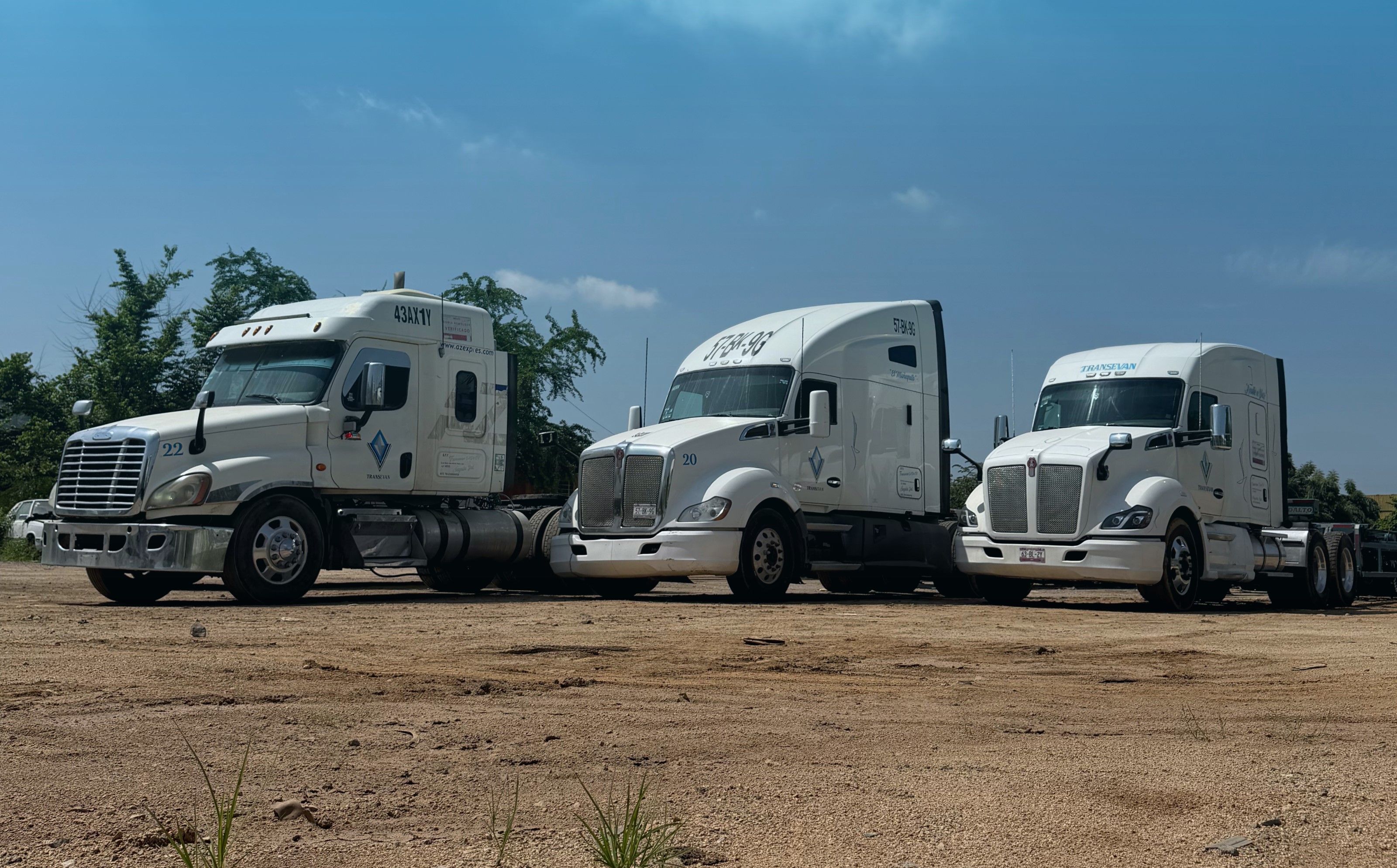 Tres tractocamiones blancos de TRANSEVAN estacionados en el patio de Manzanillo bajo un cielo azul